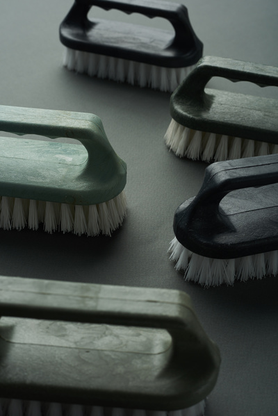 Household scrub brushes with handles in dark shades and white bristles are laid out on a black background